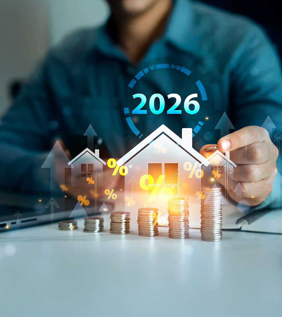 2026 real estate market concept with house icon, rising coin stacks, percentage symbols and a person working at a desk with a laptop.