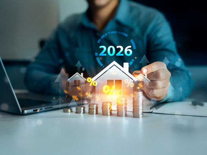 Vastgoedmarktconcept voor 2026 met een huisicoon, stijgende stapels munten, percentagesymbolen en een persoon die aan een bureau met een laptop werkt.