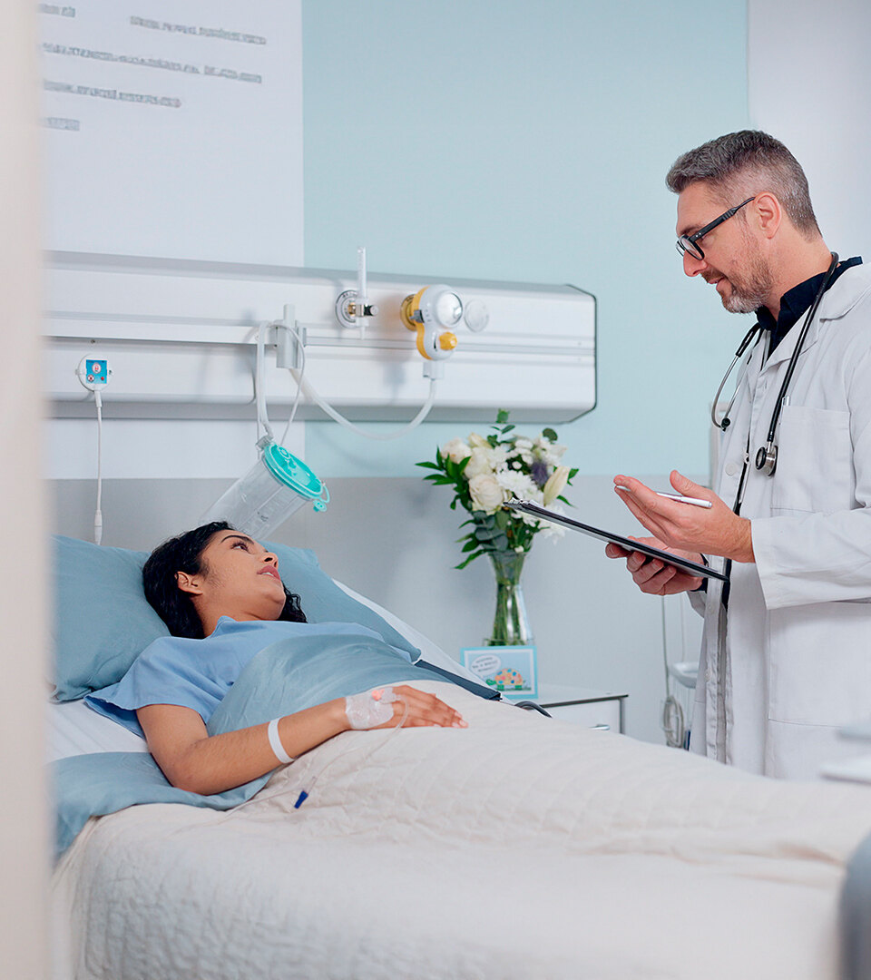 Doctor speaking with a patient lying in a hospital bed in a bright private room.