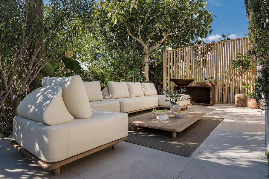Espace lounge dans un jardin privé d’une maison mitoyenne du Golden Mile de Marbella, avec canapés d’extérieur rembourrés, table basse en bois, végétation luxuriante et écran d’intimité moderne.
