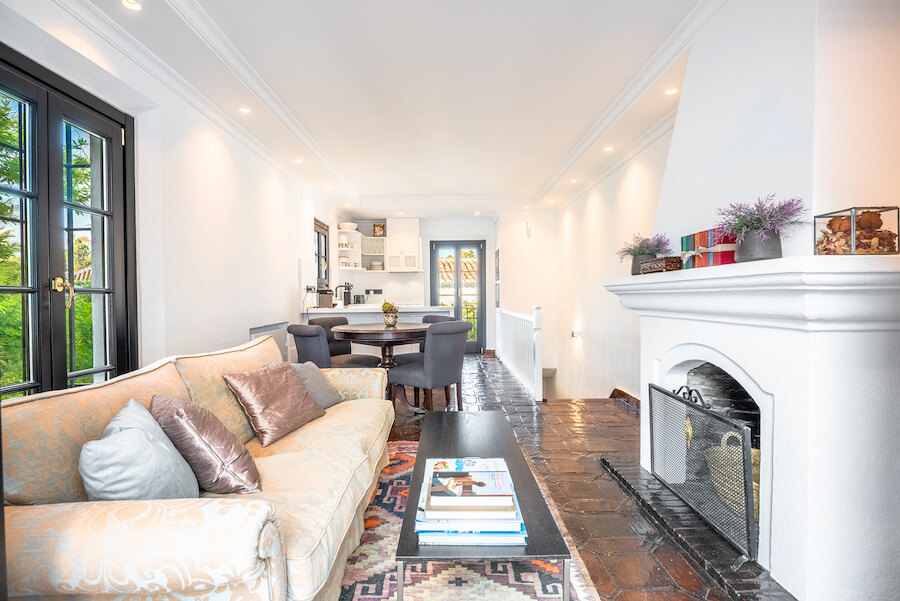 Salon lumineux avec cheminée et sols en terre cuite dans une maison mitoyenne sur le Golden Mile de Marbella, comprenant un canapé cosy, une table basse, un espace salle à manger et une cuisine ouverte.