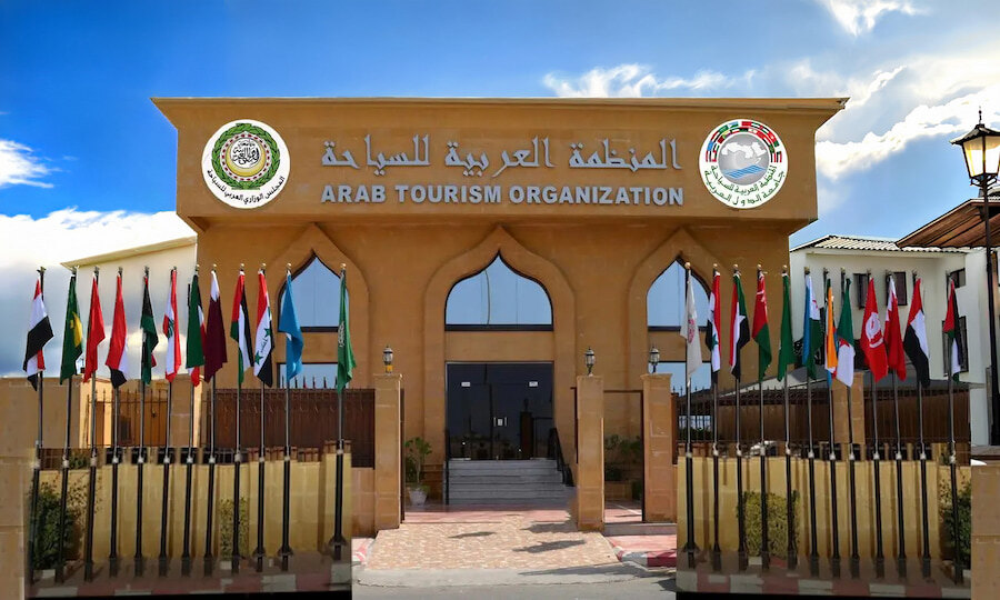Main entrance of the Arab Tourism Organization building, featuring Arabic and English signage above the gateway and a row of national flags displayed along both sides of the entrance.