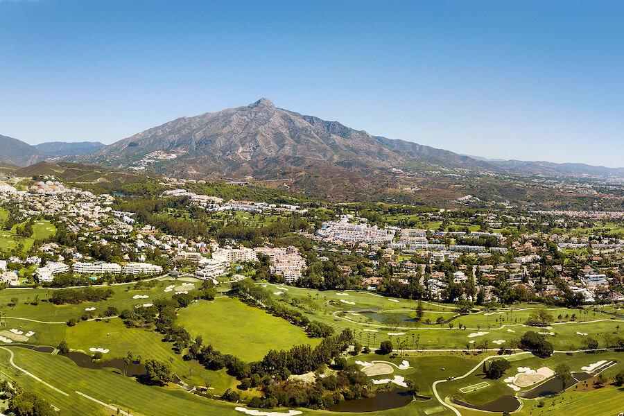 Panoramic view of Marbella’s golf valley with manicured fairways and residential areas, set beneath La Concha mountain under a clear blue sky.