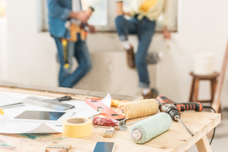 Renovation tools and materials on a worktable with construction workers in the background during an interior refurbishment.