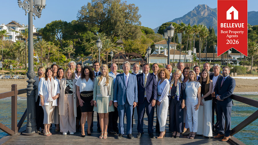 Group of real estate professionals standing on a wooden pier in Marbella with La Concha mountain in the background, featuring a “Bellevue Best Property Agents 2026” badge in the top right corner.