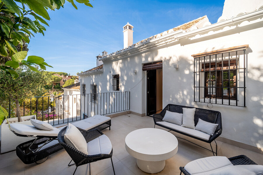 maisons mitoyennes. Terrasse privée à Lomas Pueblo, Marbella, avec façades blanchies à la chaux, grilles en fer forgé aux fenêtres, salon extérieur et vues sur des jardins luxuriants sous un ciel bleu.