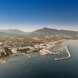 Panoramisch luchtzicht op de jachthaven van Puerto Banús en de kustlijn van Marbella, met de Middellandse Zee op de voorgrond en de berg La Concha onder een heldere blauwe lucht.