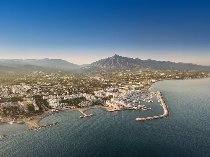 Aerial panoramic view of Puerto Banús marina and Marbella’s coastline, with the Mediterranean Sea in the foreground and La Concha mountain under a clear blue sky.