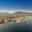 Aerial panoramic view of Puerto Banús marina and Marbella’s coastline, with the Mediterranean Sea in the foreground and La Concha mountain under a clear blue sky.
