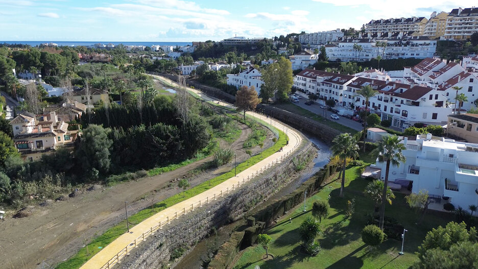 Luftaufnahme der neuen Flusspromenade von Marbella mit gepflastertem Weg, Geländern, nahegelegenen Wohnhäusern und dem Mittelmeer im Hintergrund.