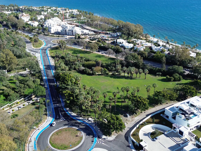 Luftaufnahme der Küstenregion von Marbella mit einem landschaftlich gestalteten Park, palmengesäumten Alleen, modernen Wohngebäuden und dem Mittelmeer im Hintergrund.