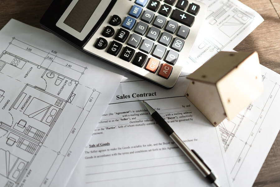 Documento de contrato de compraventa con una calculadora, un bolígrafo, una maqueta de vivienda y planos arquitectónicos, que representan la fijación de precios, el análisis financiero y las transacciones inmobiliarias.