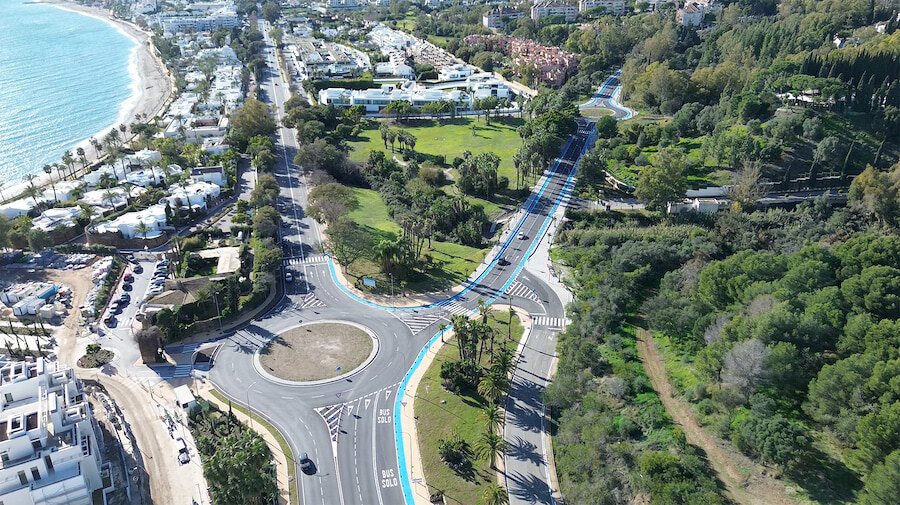 Vista aérea de la carretera de Istán renovada en Marbella, con una rotonda moderna, carriles bici azules continuos, pasos de peatones, zonas verdes ajardinadas y la costa mediterránea en las inmediaciones