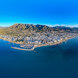 Aerial panoramic view of Marbella’s coastline with the city, marina and mountains behind, bordered by the Mediterranean under a clear blue sky.
