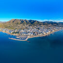 Aerial panoramic view of Marbella’s coastline with the city, marina and mountains behind, bordered by the Mediterranean under a clear blue sky.
