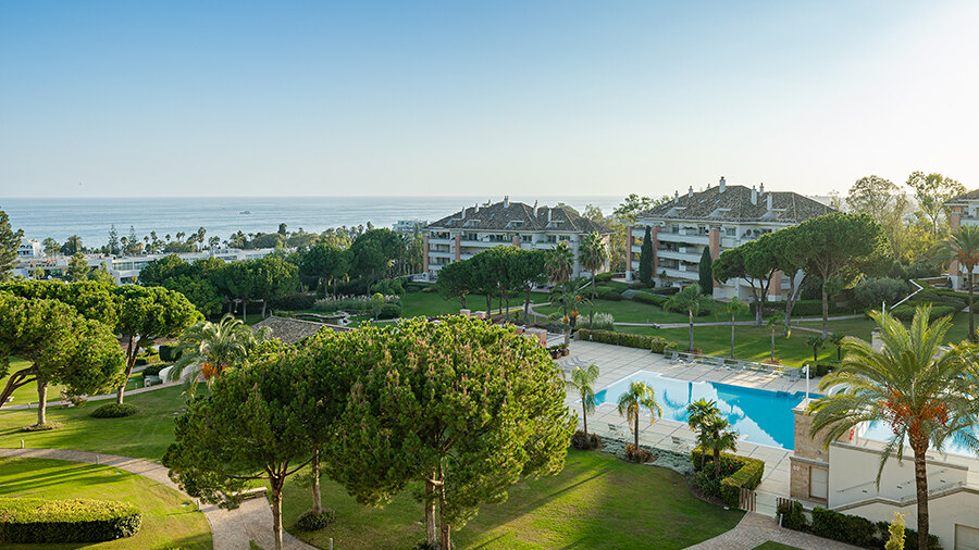 Communal pool area at Urbanización La Trinidad in Marbella, surrounded by trees and offering serene sea views.