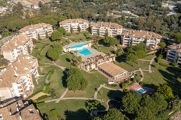 Aerial view of La Trinidad’s U-shaped layout with a communal pool and mountain views, surrounded by lush greenery.