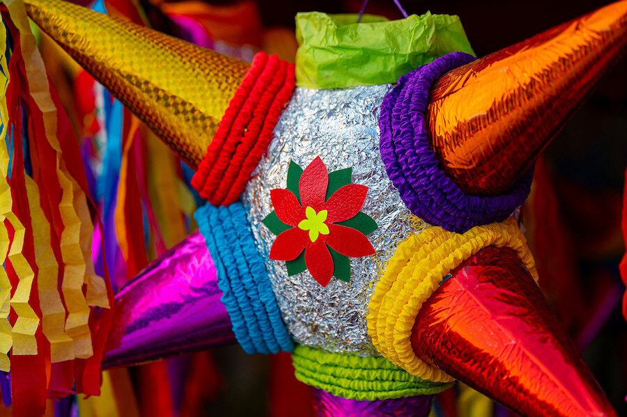 Colourful star-shaped Christmas piñata decorated with shiny foil, bright paper cones and a red poinsettia motif.