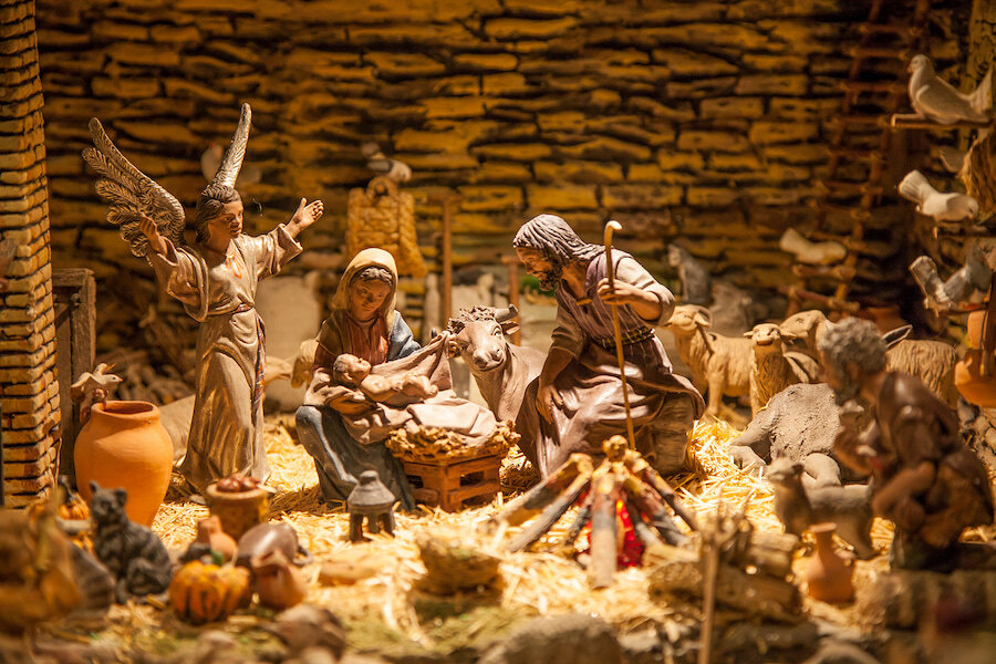 Traditional Nativity scene with Mary, Joseph and baby Jesus surrounded by an angel, shepherds and animals in a warmly lit stable.