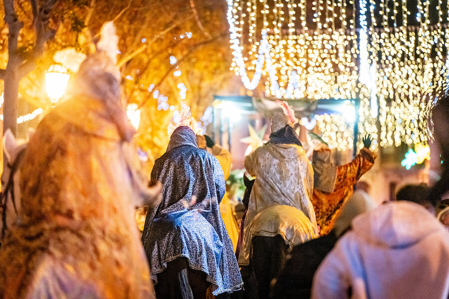 Three Kings riding on horseback in a Spanish Christmas parade at night under sparkling festive lights.