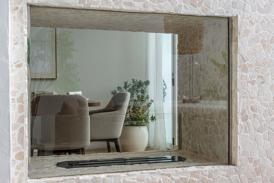 Close-up of a stone-framed glass feature at Casa Marisal, revealing a view into the elegant dining area with upholstered chairs and indoor plants.