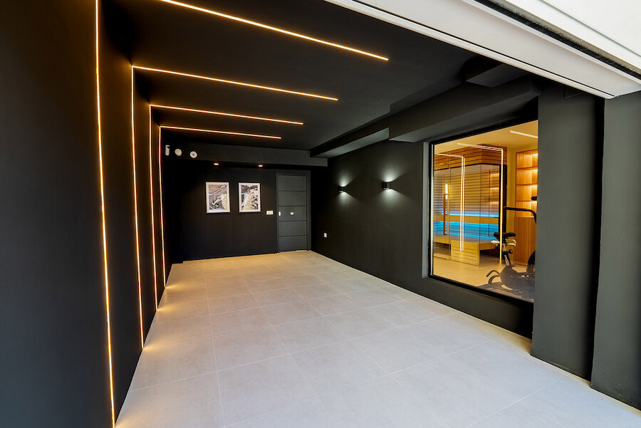 Sleek modern interior space at Casa Marisal featuring black walls with integrated LED lighting, large floor tiles, and a window revealing the home gym and spa area.