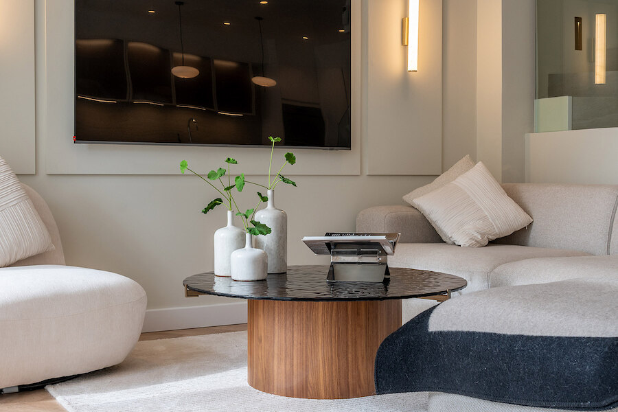 Contemporary living area at Casa Marisal featuring a round wood-and-stone coffee table, neutral curved sofas, and a wall-mounted TV with soft ambient lighting.