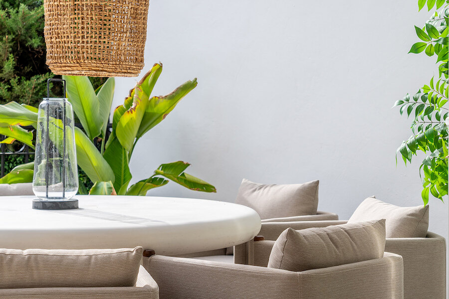 Outdoor dining area at Casa Marisal featuring cushioned chairs, a round white table, a woven pendant light, and lush tropical plants.