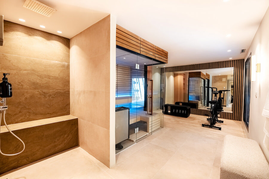 Luxury wellness area at Casa Marisal featuring a spacious walk-in shower, glass-enclosed sauna with soft lighting, fitness equipment, and contemporary wood and stone finishes.