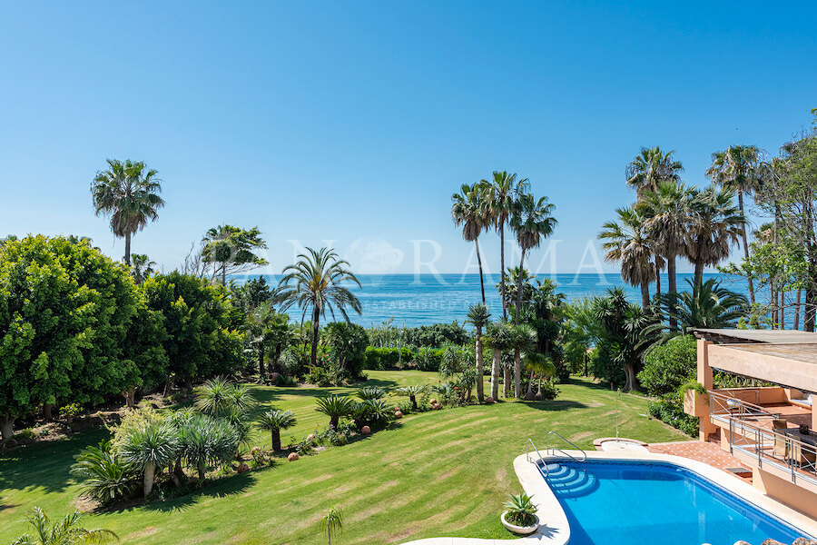 Üppiger Garten direkt am Meer mit gepflegtem Rasen, hohen Palmen und privatem Swimmingpool, mit Blick auf das Mittelmeer unter einem klaren blauen Himmel.