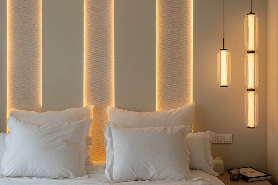 Serene bedroom at Casa Marisal featuring soft wall lighting behind textured panels, plush white bedding, and modern pendant lamps.