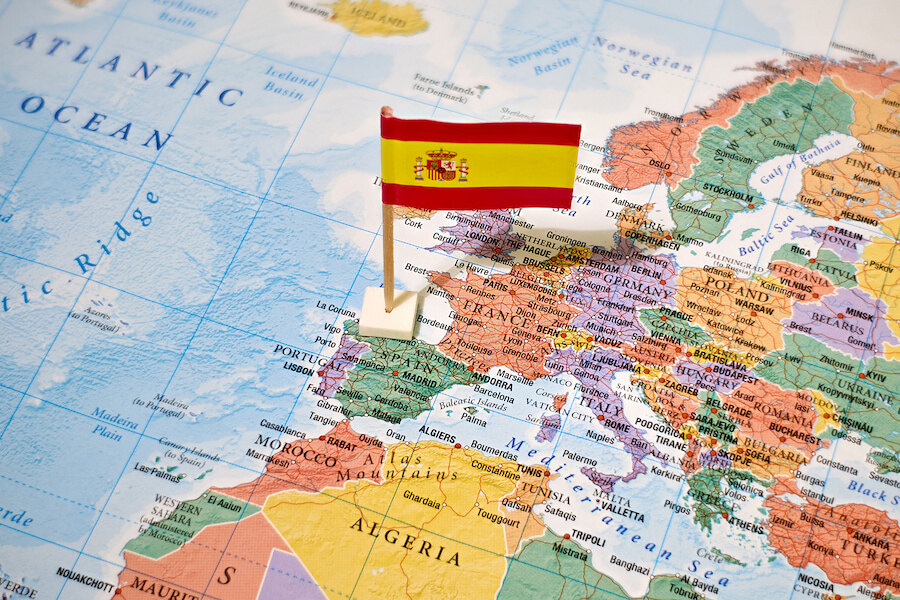 Eurozone. A small Spanish flag pinned on a map of Europe, marking the location of Spain on the Iberian Peninsula.