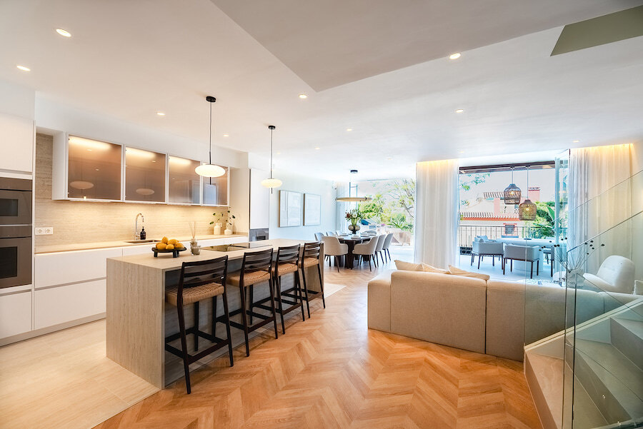 Bright open-plan kitchen, dining, and living area at Casa Marisal, featuring a large island with bar seating, modern finishes, and seamless access to a terrace with outdoor seating.