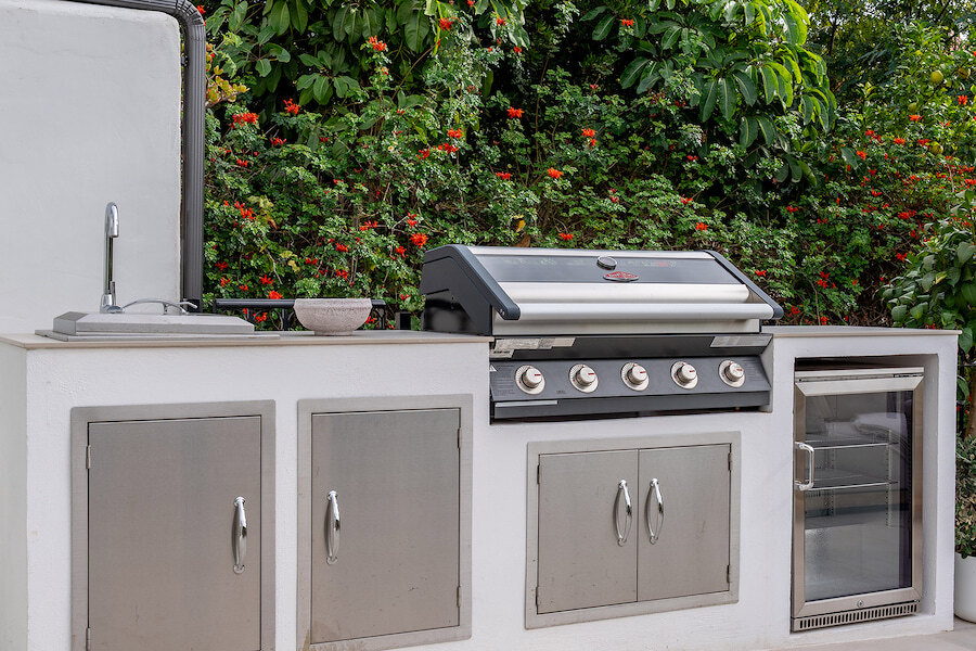 Outdoor kitchen at Casa Marisal featuring a built-in stainless steel barbecue, sink, storage cabinets, and mini fridge set against lush greenery.