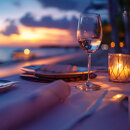 Romantic seaside dining table set for two at sunset, featuring a wine glass, lit candle, and elegant tableware with a blurred view of the ocean and colorful sky in the background.