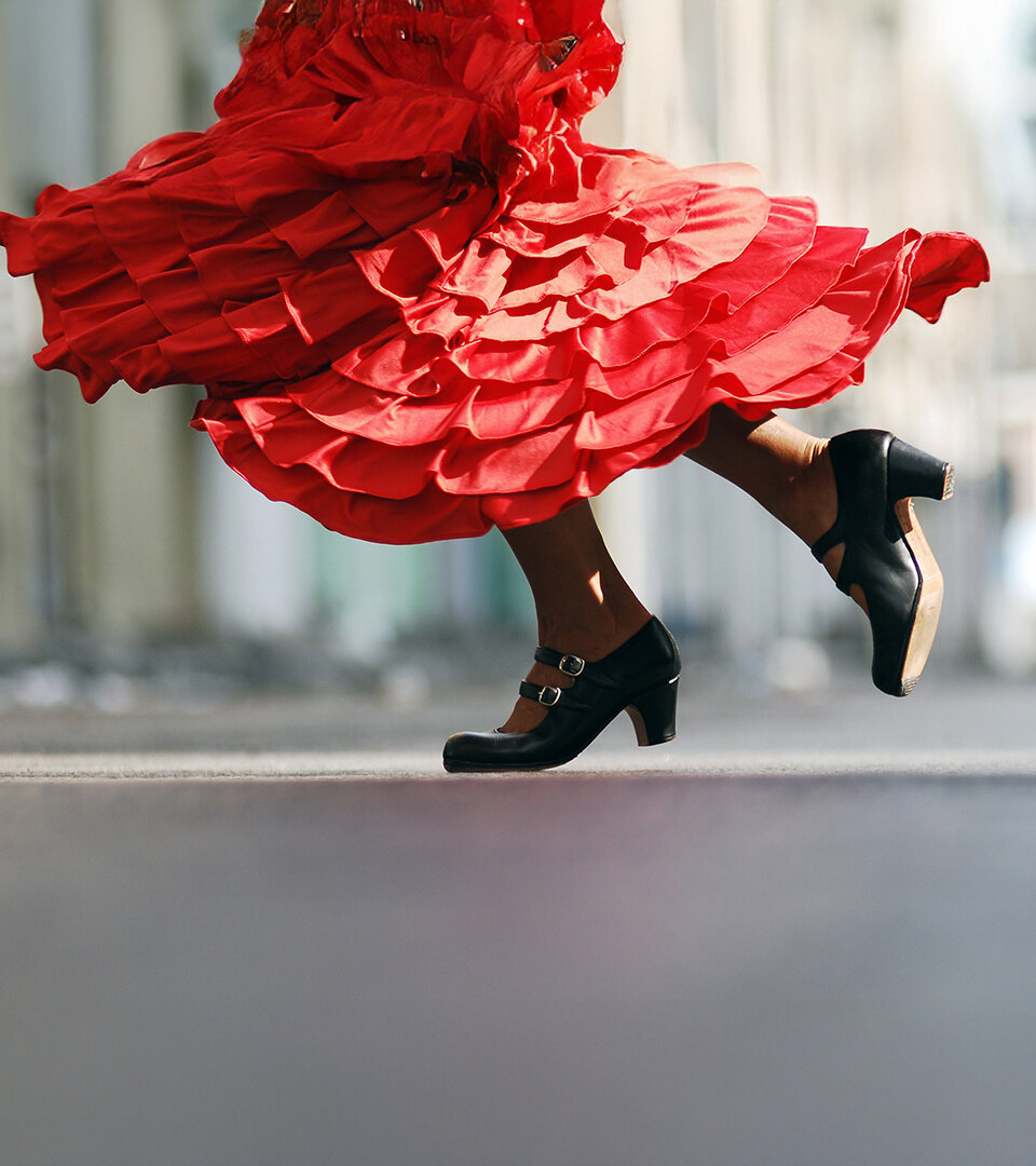 Nahaufnahme einer Flamencotänzerin in Bewegung, mit einem wirbelnden leuchtend roten Rüschenkleid und traditionellen schwarzen Stöckelschuhen mitten im Schritt, die die Energie und Eleganz des spanischen Tanzes einfängt.
