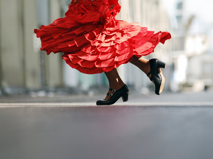 Close-up van een flamencodanseres in beweging, met een felrode geplooide jurk die heen en weer beweegt en traditionele zwarte schoenen met hakken midden in de pas, waarmee de energie en elegantie van de Spaanse dans wordt vastgelegd.
