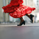 Nahaufnahme einer Flamencotänzerin in Bewegung, mit einem wirbelnden leuchtend roten Rüschenkleid und traditionellen schwarzen Stöckelschuhen mitten im Schritt, die die Energie und Eleganz des spanischen Tanzes einfängt.