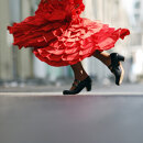 Close-up of a flamenco dancer in motion, with a vibrant red ruffled dress swirling and traditional black heeled shoes mid-step, capturing the energy and elegance of Spanish dance.