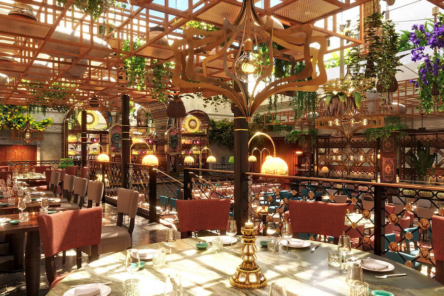 Interior of Coya Marbella restaurant at Puente Romano, featuring elegant dining tables set with glassware and plates, surrounded by warm lighting, lush greenery, and intricate decorative elements under a wooden lattice ceiling.