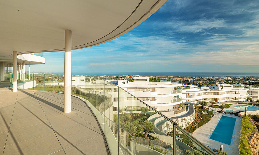 Geräumige, geschwungene Terrasse im The View Marbella, einer luxuriösen Wohnanlage mit Glasgeländern und Panoramablick über das Mittelmeer, angelegten Gärten und einem großen Gemeinschaftspool.