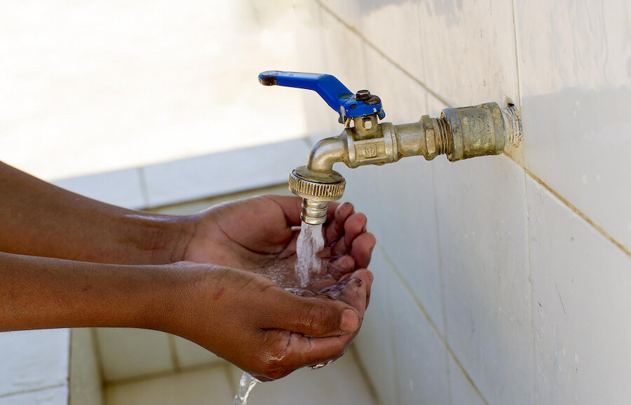 Close-up van handen die schoon stromend water uit een buitenkraan aan de muur met een blauwe hendel halen.