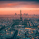 Vista aérea de París al atardecer con la Torre Eiffel en el centro y el horizonte de La Défense al fondo bajo un cielo espectacular.