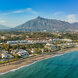 Vue aérienne du Golden Mile de Marbella, présentant des villas de luxe en bord de mer, le complexe Puente Romano et la toile de fond de la montagne La Concha sous un ciel bleu clair.