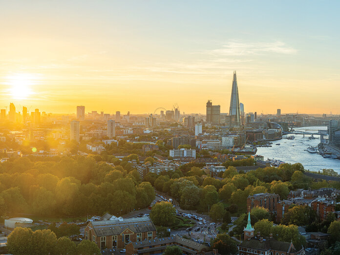 Atemberaubender Panoramablick auf London bei Sonnenuntergang mit The Shard, der Themse, dem London Eye und einer in goldenes Licht getauchten Stadtlandschaft mit üppig grünen Bäumen und historischen Gebäuden im Vordergrund.