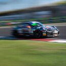A black race car speeding around a track during a motorsport event, captured with motion blur to emphasise its high velocity and dynamic movement.
