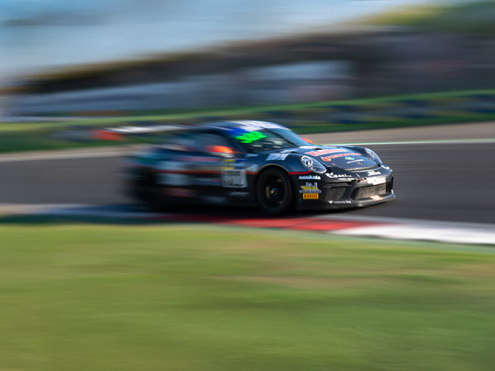 Een zwarte racewagen rijdt tijdens een motorsport-evenement met hoge snelheid over een circuit. De beelden zijn vastgelegd met bewegingsonscherpte om de hoge snelheid en dynamische bewegingen te benadrukken.