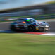 Ein schwarzes Rennauto, das während eines Motorsport-Events über eine Rennstrecke rast, aufgenommen mit Bewegungsunschärfe, um seine hohe Geschwindigkeit und dynamische Bewegung hervorzuheben.