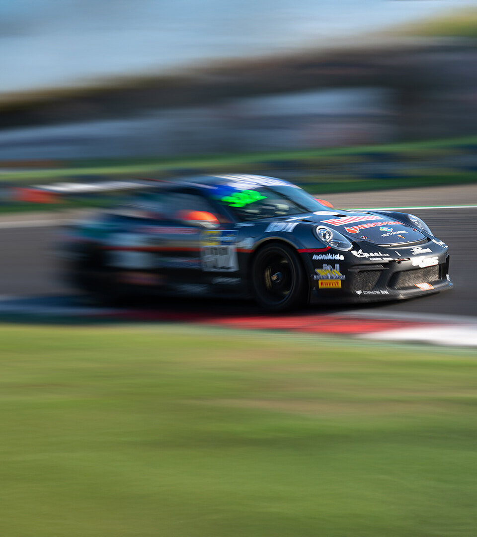 Ein schwarzes Rennauto, das während eines Motorsport-Events über eine Rennstrecke rast, aufgenommen mit Bewegungsunschärfe, um seine hohe Geschwindigkeit und dynamische Bewegung hervorzuheben.