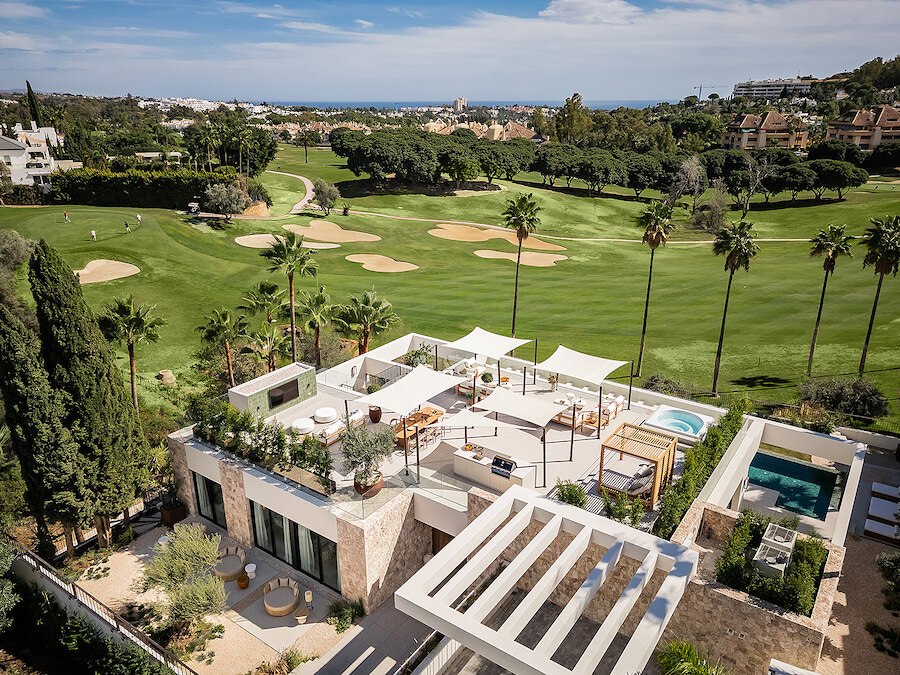villas en primera línea de golf. Vista aérea de una lujosa villa en primera línea de golf en el campo de Los Naranjos en Marbella, que cuenta con una espectacular terraza en la azotea con zonas de estar, comedor al aire libre, jacuzzi y vistas panorámicas al mar y al campo de golf.